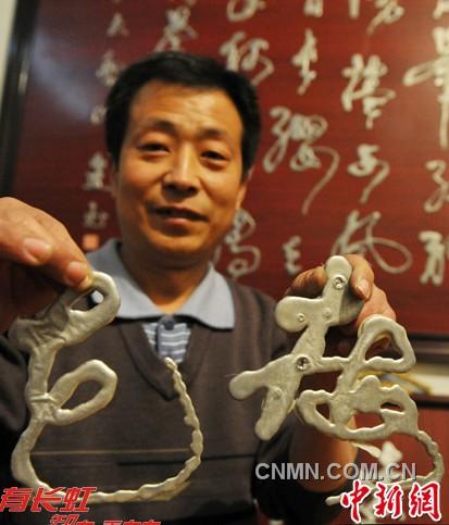 图为高建书展示金属液体书写的梅、花字。